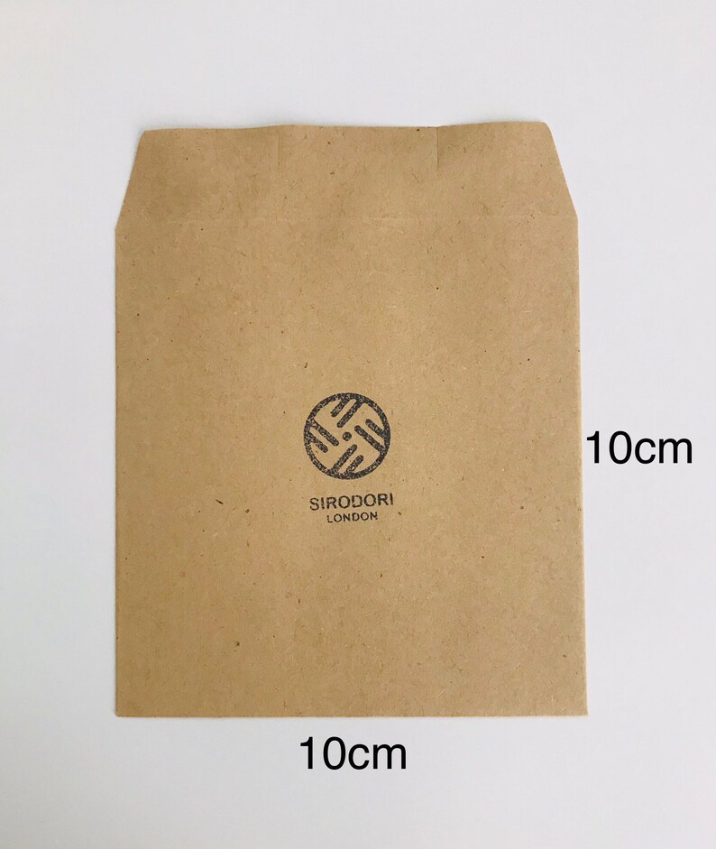May include: A brown paper envelope, 10cm x 10cm, with a circular logo and the text "SIRODORI LONDON" printed in black. The envelope is rectangular with a folded top flap.