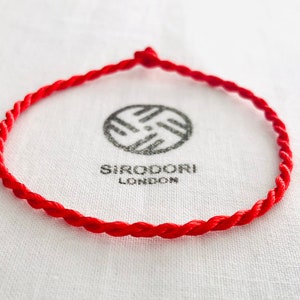 May include: A red braided string bracelet with a knot at the end.