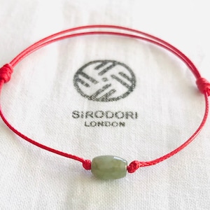May include: A red string bracelet with a light green jade bead. The bracelet is tied with a knot at each end.