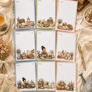 May include: Nine notepads with illustrated cottagecore designs. Each notepad has a white interior with the word "notes" at the top and a heart symbol. The notepads have blue, green, and pink borders with various illustrations.