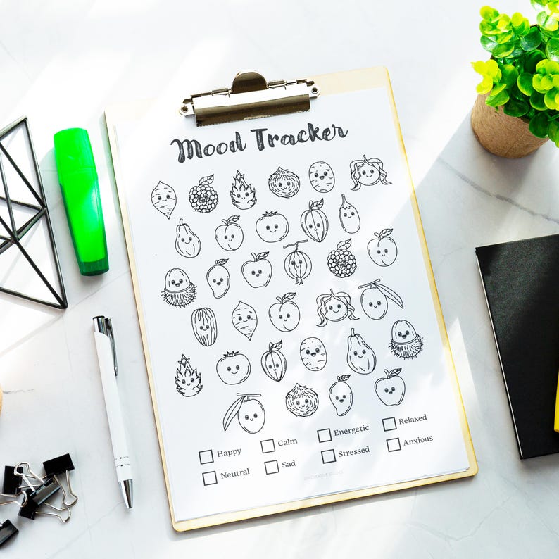 May include: A wooden clipboard with a printed "Mood Tracker" sheet featuring illustrated fruit and vegetable faces. The sheet includes checkboxes for tracking emotions like happy, calm, and stressed. A green highlighter and a white pen are also visible.