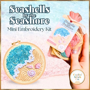 May include: A mini embroidery kit with a seashell and ocean wave design. The kit includes a hoop, embroidery floss, and a needle. The kit is packaged in a clear plastic bag with a pink drawstring bag. The bag has the text "Seashells by the Seashore Mini Embroidery Kit" printed on it.