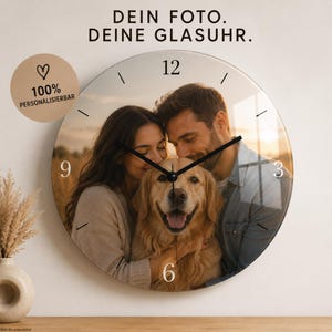 Könnte beinhalten: Eine runde Wanduhr aus Glas mit einem individuellen Foto von zwei Personen und einem Golden Retriever. Das Zifferblatt zeigt die Zahlen 3, 6, 9 und 12 sowie schwarze Zeiger. Über der Uhr steht der Text DEIN FOTO. DEINE GLASUHR.