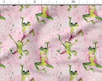 May include: A pink fabric with a repeating pattern of green frogs in various poses. The frogs are painted in a watercolor style with pink accents. The background is a light pink with white speckles.