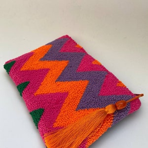 May include: A colourful clutch purse with a chevron pattern in shades of pink, orange, purple, and green. The purse has a tassel and a beaded zipper pull.