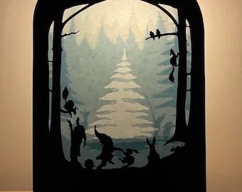 Könnte beinhalten: Eine schwarze Silhouette-Waldszene mit hellblauem Hintergrund. Die Szene zeigt Bäume, Tiere und Figuren, darunter ein Eichhörnchen, Vögel und Kaninchen. Das Kunstwerk wird in einem Holzrahmen präsentiert.