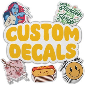 May include: A collection of custom decals featuring various designs, including a hot dog with a smiley face, a cherry blossom branch, a smiley face with the text "Happy Times", and a design with the text "Garden More Stress Less". The decals are stacked on top of each other and have a white background with a textured paper-like finish. The text "CUSTOM DECALS" is in large, yellow, bubble letters.