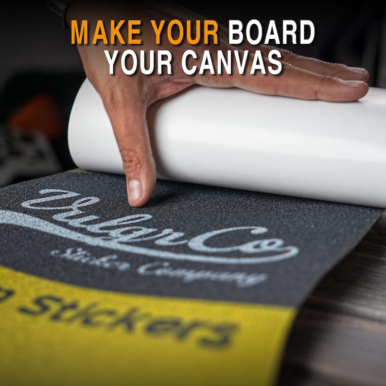 May include: A hand applying a white roll of material onto a black skateboard grip tape. The grip tape has the text "Vulgar Co Sticker Company" in white. The text "MAKE YOUR BOARD YOUR CANVAS" is in the top left corner.