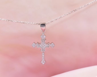 May include: A silver necklace with a small, sparkling, cross pendant. The cross is adorned with tiny, clear stones.