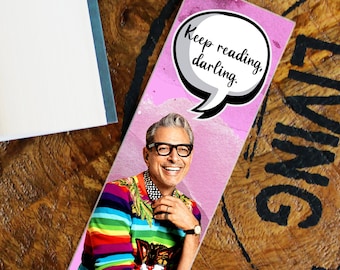 Puede incluir: Un marcapáginas rosa con un bocadillo que dice "Sigue leyendo, cariño." El marcapáginas presenta a un hombre con un suéter a rayas de colores y un gráfico de un gato.