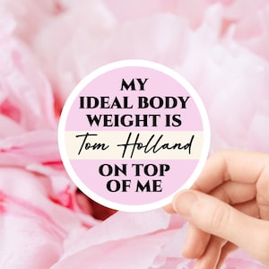 May include: A pink and white round sticker with the text "My ideal body weight is Tom Holland on top of me".