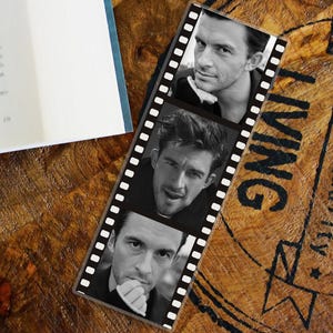 May include: A black and white bookmark with three portraits of a man in a film strip design. The bookmark is on a wooden surface with the word "LIVING" printed on it.