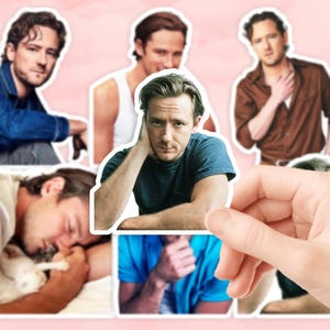 Puede incluir: Una mano sosteniendo una hoja de pegatinas con múltiples imágenes de un hombre en varias poses y atuendos. Las imágenes incluyen una chaqueta vaquera, una camisa marrón y una camiseta azul. El fondo es de color rosa claro.