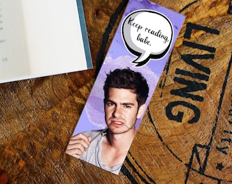May include: A purple and white bookmark with a watercolor background featuring a man with brown hair and a speech bubble that says "Keep reading, babe."