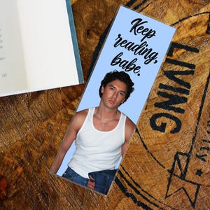 Könnte beinhalten: Ein rechteckiges Lesezeichen mit hellblauem Hintergrund, schwarzem Text "Keep reading, babe." und einem Foto einer Person mit dunklem Haar, die ein weißes Unterhemd und eine silberne Halskette trägt und eine blaue Jeans hält.