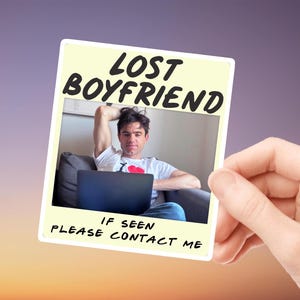 Può includere: Una fotografia, tenuta in mano, raffigurante un uomo seduto su un divano con un computer portatile. La foto ha il testo "LOST BOYFRIEND" e "IF SEEN PLEASE CONTACT ME". L'uomo indossa una maglietta bianca con un cuore.