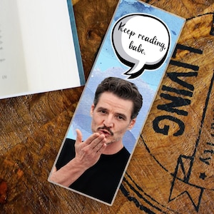 May include: A rectangular bookmark featuring a portrait of a man blowing a kiss. The bookmark has a speech bubble with the text "Keep reading, babe." The background is a watercolor design with blue and white hues.