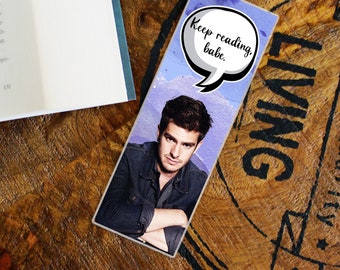 May include: A blue and white bookmark with a watercolor background featuring a man with brown hair and a speech bubble that says "Keep reading, babe."