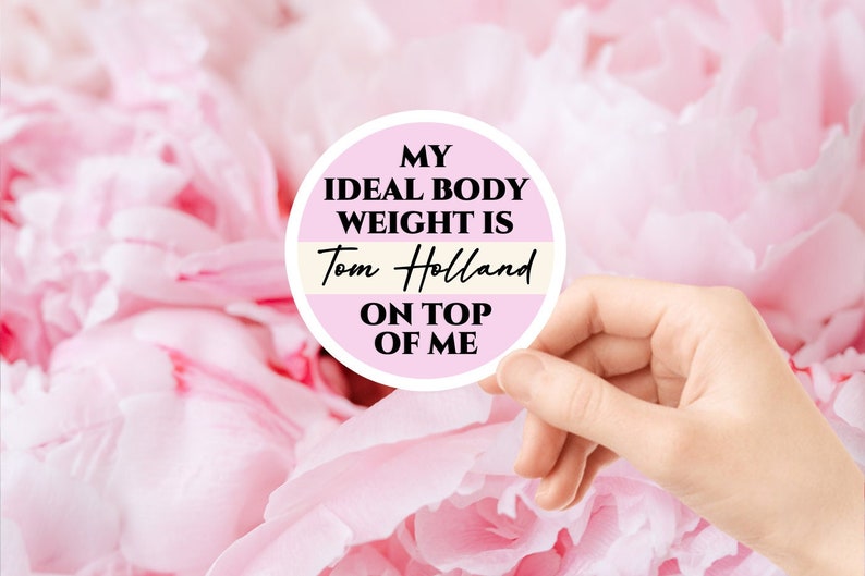 May include: A pink and white round sticker with the text "My ideal body weight is Tom Holland on top of me".