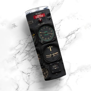 May include: A stainless steel tumbler featuring a vintage aircraft instrument panel design. The black panel displays gauges, dials, and the text "GYRO COMPASS" and "RADIO COMPASS". The tumbler is cylindrical and has a silver lid.