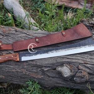 May include: A large, black,  machete with a wooden handle and a brown leather sheath. The machete is resting on a piece of wood with the sheath beside it. The text "RESIDENCE CO." is visible on the blade.