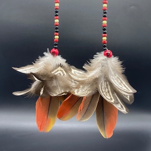 May include: A pair of long, beaded earrings with a cluster of brown and orange feathers at the bottom. The beads are black, red, and cream.
