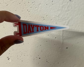 May include: A blue and red pennant with the word "DAYTON" printed in white letters.
