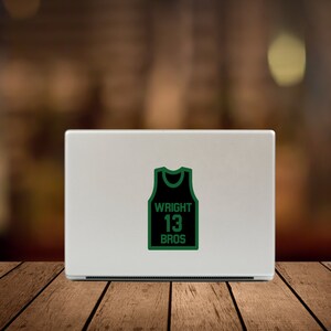 May include: A green and black basketball jersey sticker with the text "WRIGHT 13 BROS" on a silver laptop.