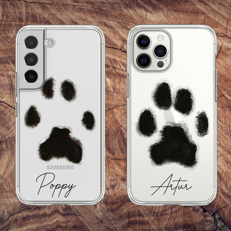 May include: Clear phone cases with a black paw print design. One case is for a Samsung phone and the other is for an iPhone. The Samsung case has the name "Poppy" in a script font. The iPhone case has the name "Artur".