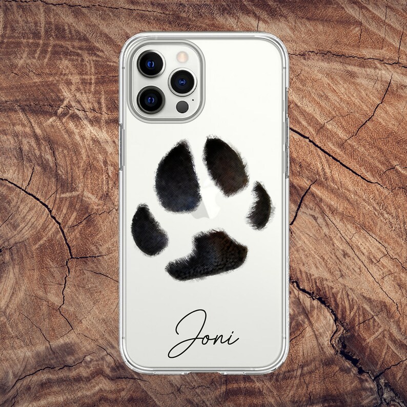 May include: Clear phone case featuring a black paw print design and the name "Joni" in a cursive font. The case is designed to fit a smartphone and has a clear back.