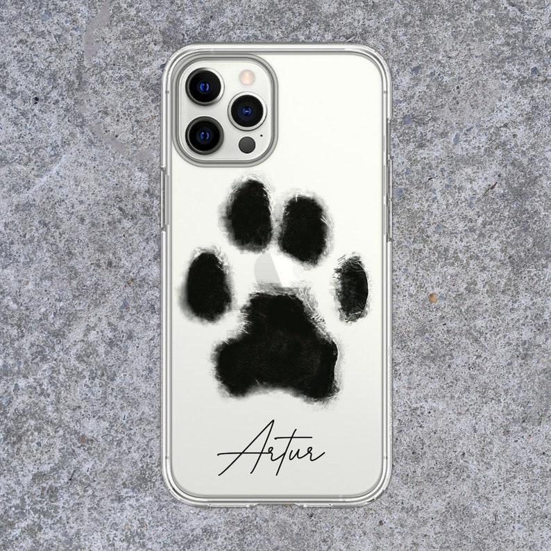 May include: Clear phone case featuring a large, black paw print design. The name "Artur" is written in a cursive font below the paw print. The case is designed to fit a smartphone.