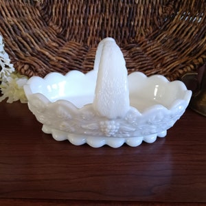 May include: White milk glass bowl with a handle in the shape of a grapevine. The bowl has a scalloped edge and is decorated with a grapevine design.