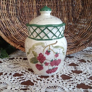 May include: A ceramic jar with a lid, featuring a white base with a crackle finish. The jar is adorned with a green lattice design around the rim and a green knob on the lid. Red floral and green vine motifs decorate the jar's surface.