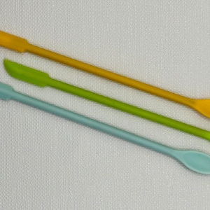 May include: Three silicone spoons in different colors: yellow, green, and light blue. The spoons are long and narrow with rounded ends.