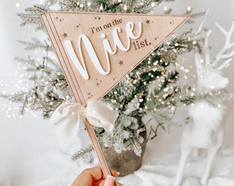 May include: Wooden Christmas tree topper with a white ribbon and the text "I'm on the Nice List."