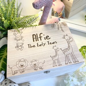 May include: A wooden keepsake box with a light wood finish. The box has a hinged lid and a latch. The lid is engraved with the text "Alfie The Early Years" and features a variety of animal illustrations, including monkeys, giraffes, and lions.