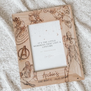 Op de afbeelding: Een houten fotolijst met een opening van 13x18 cm, met een ontwerp van verschillende Marvel-superhelden, waaronder Iron Man, Captain America, Thor, Hulk en Spiderman. De lijst is gepersonaliseerd met de naam "Archie's" en de tekst "Disney Adventure - Januari 2025". De lijst bevat ook de quote "Het zijn de kleine herinneringen die een leven lang meegaan."