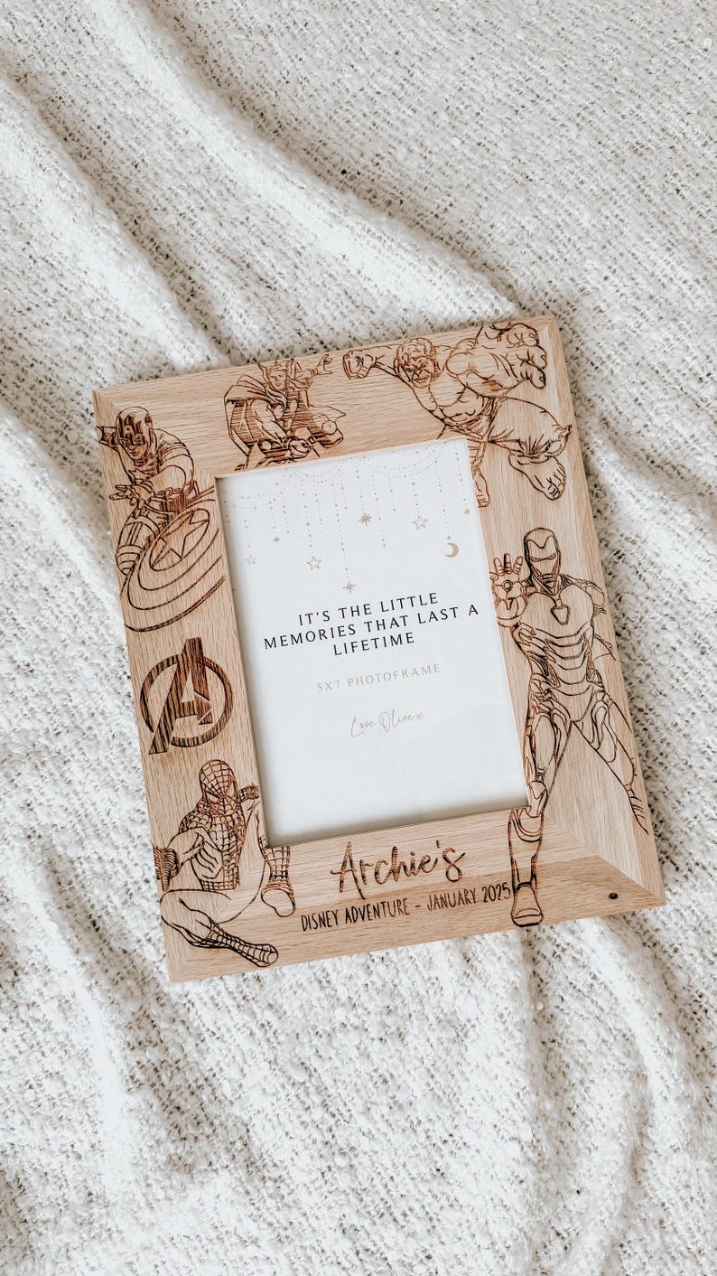 Op de afbeelding: Een houten fotolijst met een opening van 13x18 cm, met een ontwerp van verschillende Marvel-superhelden, waaronder Iron Man, Captain America, Thor, Hulk en Spiderman. De lijst is gepersonaliseerd met de naam "Archie's" en de tekst "Disney Adventure - Januari 2025". De lijst bevat ook de quote "Het zijn de kleine herinneringen die een leven lang meegaan."