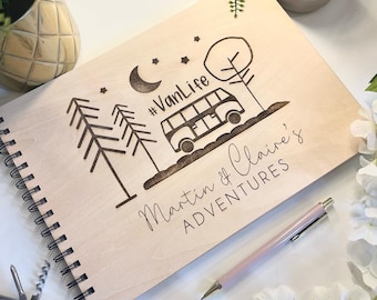 May include: A wooden journal with a spiral binding, featuring a laser-engraved design of a van, trees, stars, and a crescent moon. The text "#VanLife" and "Martin & Claire's Adventures" is also engraved on the cover.