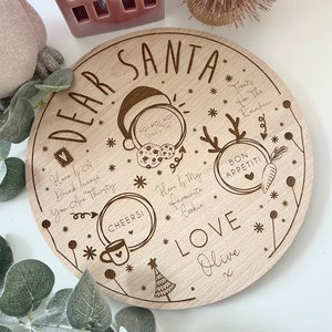 May include: A round wooden plate with a Christmas theme. It has the words "Dear Santa" at the top and "Love Olive" at the bottom. There are several other phrases and images on the plate, including "Ho! Ho! Ho!" and "Here is my favorite cookie".