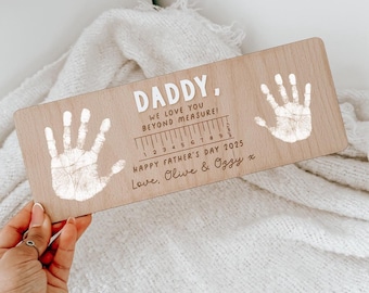 May include: Wooden plaque with handprints and the text "DADDY, WE LOVE YOU BEYOND MEASURE! HAPPY FATHER'S DAY 2025 Love, Olive & Ozzy x". The plaque has a ruler design with inch markings.