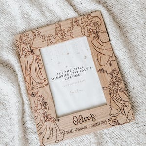 May include: A wooden photo frame featuring a Disney princess theme. The frame is decorated with images of princesses such as Belle, Ariel, and Snow White. The frame is 5x7 inches and includes the text "It's the little memories that last a lifetime" and "Olive's Disney Adventure - January 2025".