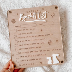 May include: A wooden Easter bucket list sign with a white bunny cutout. The list includes activities like wearing bunny ears, eating chocolate, and going on an Easter egg hunt.