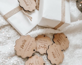May include: Seven wooden gift tags with a scalloped edge and a string attached. Each tag has the text "Olive, something to..." followed by a different word, such as "read", "want", "love", "need", "play", "share", and "from Santa".