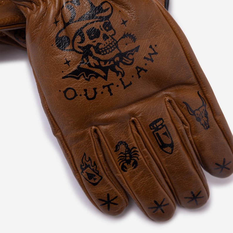 May include: Brown leather gloves with black tattoo-style designs. The gloves feature a skull wearing a hat, the word "OUTLAW", and other symbols. The gloves are made of a soft leather material.