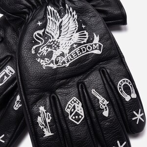 May include: Black leather gloves with white graphic designs. The gloves feature an eagle with the word "FREEDOM", a cactus, dice, a revolver, and a horseshoe. The gloves are designed for protection and style.