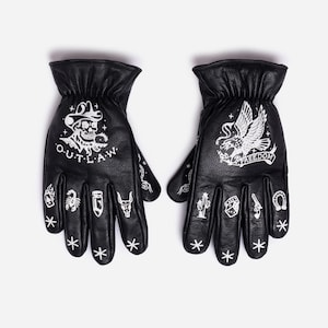 May include: Black leather gloves with white graphic designs. One glove features a skull with a cowboy hat and the word "OUTLAW". The other glove displays an eagle and the word "FREEDOM". Additional small graphics include a scorpion, cactus, and horseshoe.