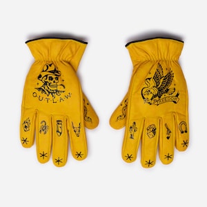May include: A pair of yellow leather work gloves with black trim. The left glove features a skull with the word "OUTLAW", and the right glove has an eagle with the word "FREEDOM". Both gloves have various tattoo-style designs.
