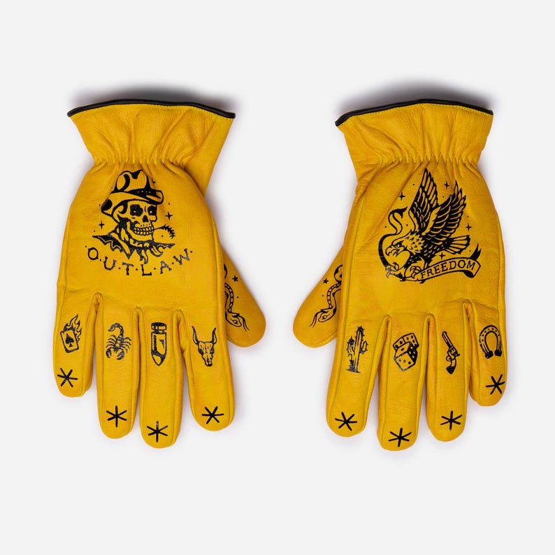 May include: A pair of yellow leather work gloves with black trim. The left glove features a skull with the word "OUTLAW", and the right glove has an eagle with the word "FREEDOM". Both gloves have various tattoo-style designs.