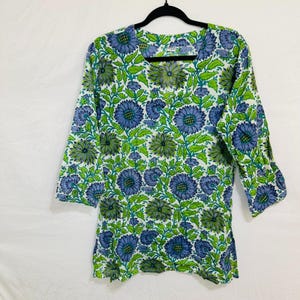 Puede incluir: Una túnica blanca con estampado floral verde y azul. La túnica tiene cuello en V y mangas tres cuartos.